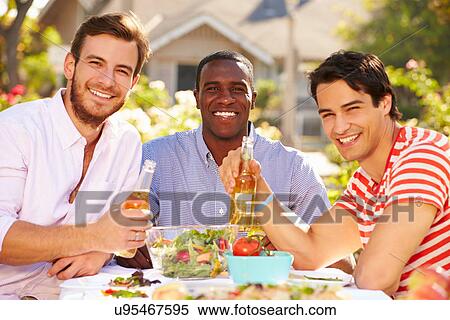 Stock Photography - Three Male Friends Enjoying Meal At Outdoor Party. Fotosearch