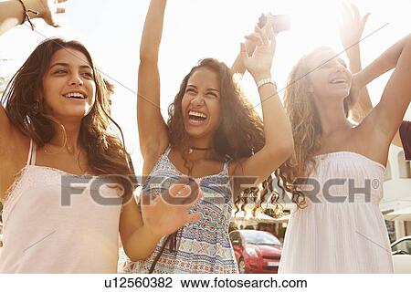 Stock Image - Three Teenage Girls Dancing Outdoors Against Sun. Fotosearch