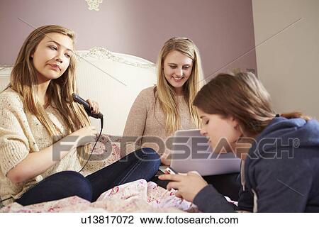 Stock Image - Three Teenage Girls Relaxing In Bedroom Together. Fotosearch