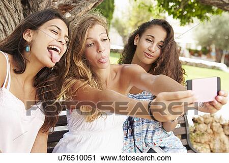 Three Teenage Girls Sitting On Bench Taking Selfie In Park View Large Photo Image Stock Image - Three Teenage Girls Sitting On Bench Taking Selfie In Park. Fotosearch