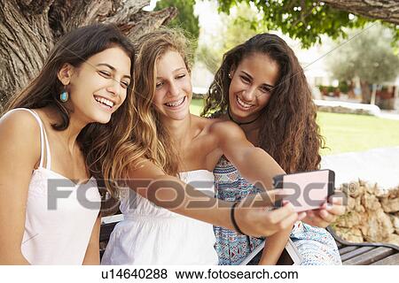Three Teenage Girls Sitting On Bench Taking Selfie In Park View Large Photo Image Stock Photo - Three Teenage Girls Sitting On Bench Taking Selfie In Park. Fotosearch