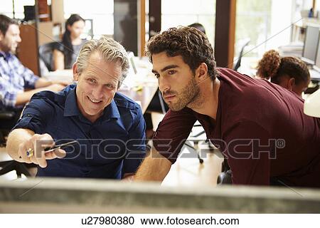 Two Colleagues Working At Desk With Meeting In Background View Large Photo Image Stock Image - Two Colleagues Working At Desk With Meeting In Background. Fotosearch