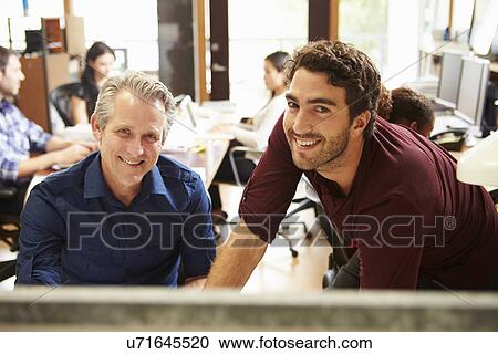 Two Colleagues Working At Desk With Meeting In Background View Large Photo Image Stock Image - Two Colleagues Working At Desk With Meeting In Background. Fotosearch