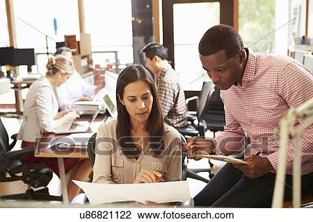 Two Colleagues Working At Desk With Meeting In Background View Large Photo Image Stock Image - Two Colleagues Working At Desk With Meeting In Background. Fotosearch