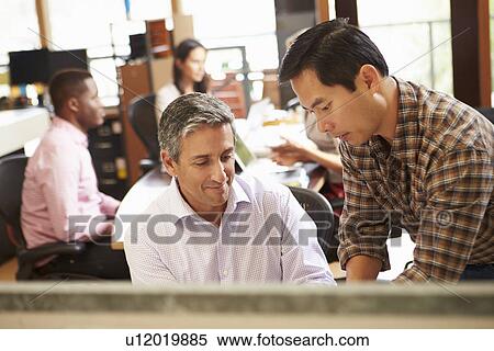 Two Colleagues Working At Desk With Meeting In Background View Large Photo Image Stock Photography - Two Colleagues Working At Desk With Meeting In Background. Fotosearch