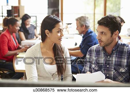 Two Colleagues Working At Desk With Meeting In Background View Large Photo Image Stock Photography - Two Colleagues Working At Desk With Meeting In Background. Fotosearch