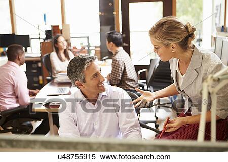 Two Colleagues Working At Desk With Meeting In Background View Large Photo Image Stock Photography - Two Colleagues Working At Desk With Meeting In Background. Fotosearch