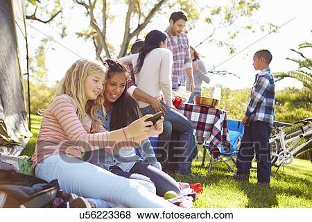 Stock Photo - Two Girls Using Mobile Phone On Family Camping Holiday. Fotosearch
