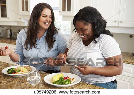 Stock Photograph - Two Overweight Women On Diet Eating Healthy Meal In Kitchen. Fotosearch
