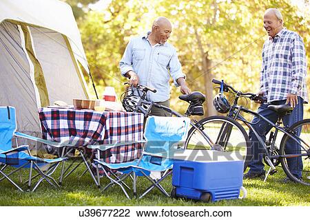 Stock Image - Two Senior Men Riding Bikes On Camping Holiday. Fotosearch