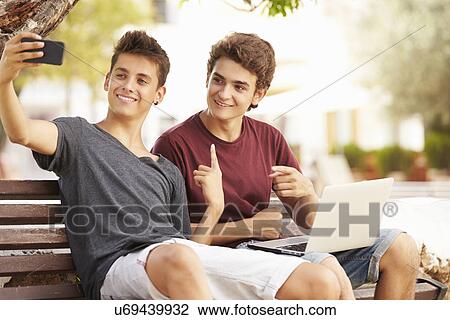Two Teenage Boys Sitting On Bench Taking Selfie In Park View Large Photo Image Stock Image - Two Teenage Boys Sitting On Bench Taking Selfie In Park. Fotosearch