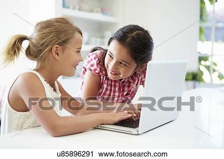 Stock Image - Two Young Girls Using Laptop At Home. Fotosearch