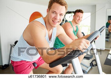 Two Young Men Training In Gym On Cycling Machines Together View Large Photo Image Stock Image - Two Young Men Training In Gym On Cycling Machines Together. Fotosearch