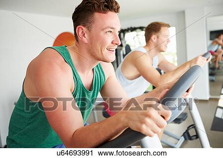 Two Young Men Training In Gym On Cycling Machines Together View Large Photo Image Stock Image - Two Young Men Training In Gym On Cycling Machines Together. Fotosearch