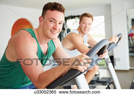 Two Young Men Training In Gym On Cycling Machines Together View Large Photo Image Stock Photography - Two Young Men Training In Gym On Cycling Machines Together. Fotosearch