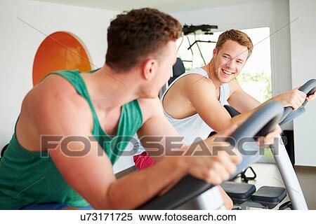 Stock Photography - Two Young Men Training In Gym On Cycling Machines Together. Fotosearch