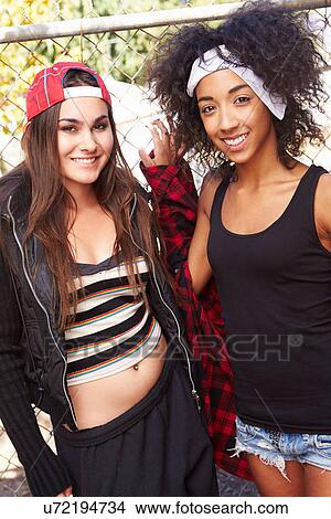 Picture - Two Young Women In Urban Setting Standing By Fence. Fotosearch