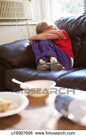 Stock Photograph - Unhappy Girl Sitting On Sofa At Home. Fotosearch