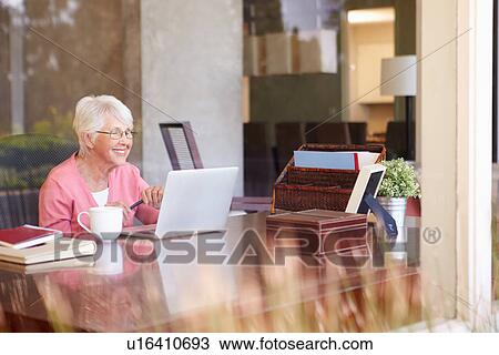 Stock Image - View Of Senior Woman Using Laptop Through Window. Fotosearch