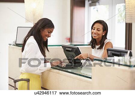 Stock Photo - Woman Checking In At Hotel Reception Using Digital Tablet. Fotosearch