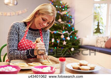 Stock Image - Woman Decorating Christmas Cookies In Kitchen. Fotosearch