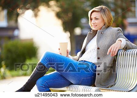 Stock Image - Woman Relaxing On Park Bench With Takeaway Coffee. Fotosearch