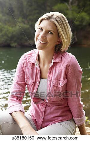 Stock Image - Woman sitting by lake. Fotosearch