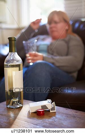 Stock Image - Woman Sitting On Sofa With Bottle Of Wine And Cigarettes. Fotosearch