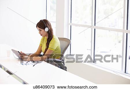 Stock Image - Woman Using Digital Tablet And Headphones In Design Studio. Fotosearch