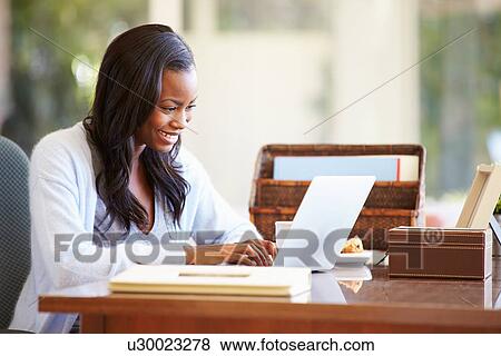 Stock Photo - Woman Using Laptop On Desk At Home. Fotosearch