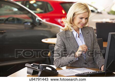 Stock Image - Woman working in car showroom. Fotosearch