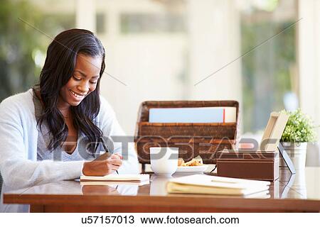 Stock Image - Woman Writing In Notebook Sitting At Desk. Fotosearch