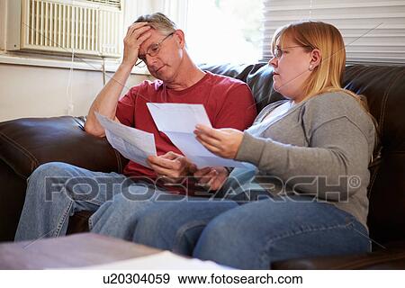 Worried Couple Sitting On Sofa Looking At Bills View Large Photo Image Stock Photo - Worried Couple Sitting On Sofa Looking At Bills. Fotosearch