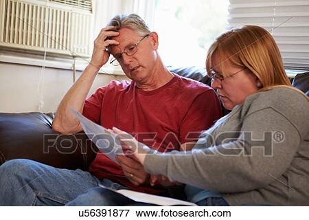 Worried Couple Sitting On Sofa Looking At Bills View Large Photo Image Stock Photo - Worried Couple Sitting On Sofa Looking At Bills. Fotosearch