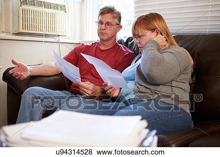 Worried Couple Sitting On Sofa Looking At Bills View Large Photo Image Stock Photo - Worried Couple Sitting On Sofa Looking At Bills. Fotosearch