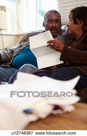 Stock Photo - Worried Senior Couple Sitting On Sofa Looking At Bills. Fotosearch