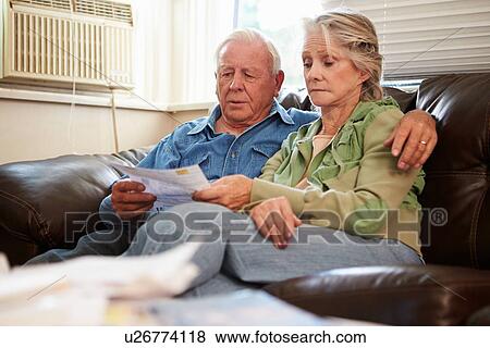 Stock Photo - Worried Senior Couple Sitting On Sofa Looking At Bills. Fotosearch