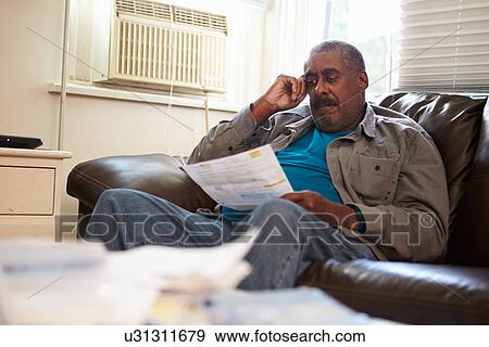 Worried Senior Man Sitting On Sofa Looking At Bills View Large Photo Image Stock Photo - Worried Senior Man Sitting On Sofa Looking At Bills. Fotosearch