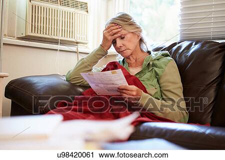 Stock Image - Worried Senior Woman Sitting On Sofa Looking At Bills. Fotosearch