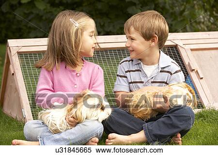 Stock Photography - Young boy and girl in garden holding guinea pigs. Fotosearch