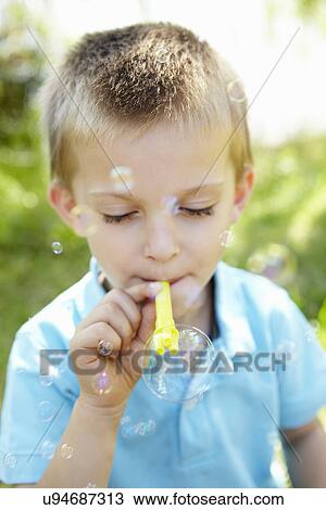Stock Image - Young boy blowing bubbles outdoors. Fotosearch