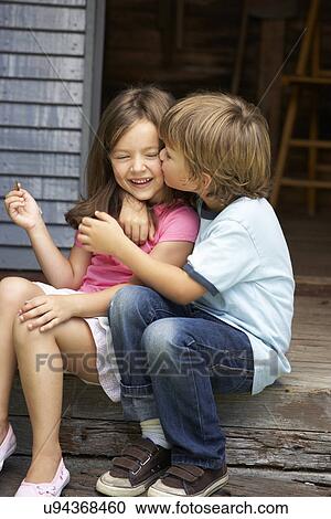 Stock Image - Young boy kissing sister on veranda. Fotosearch