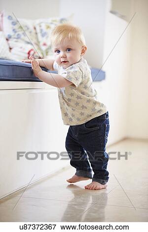 Young Boy Learning To Walk By Holding Onto Furniture View Large Photo Image Stock Photo - Young Boy Learning To Walk By Holding Onto Furniture. Fotosearch