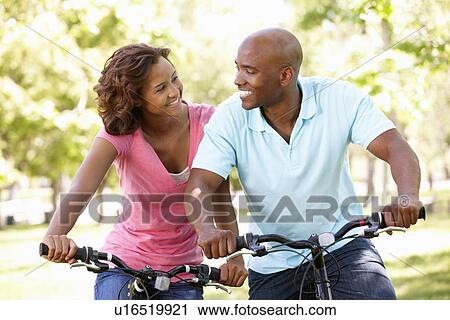 Stock Image - Young couple cycling in park. Fotosearch
