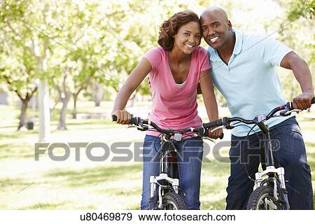 Young couple cycling in park View Large Photo Image Stock Photo - Young couple cycling in park. Fotosearch