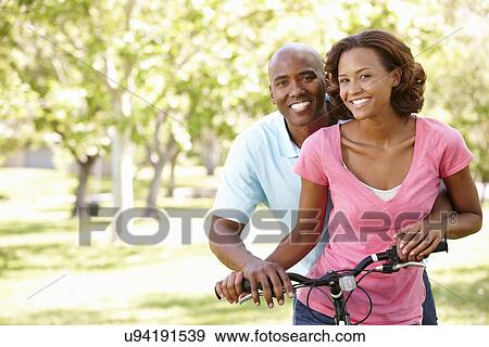 Young couple cycling in park View Large Photo Image Stock Photo - Young couple cycling in park. Fotosearch