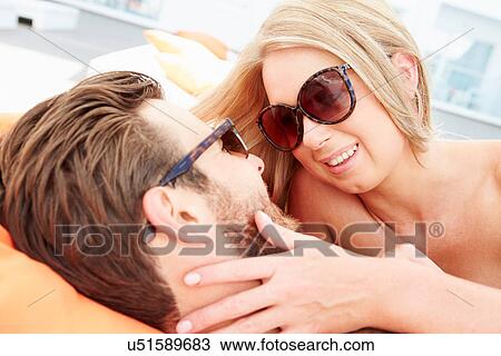 Stock Image - Young Couple On Holiday Relaxing By Swimming Pool. Fotosearch