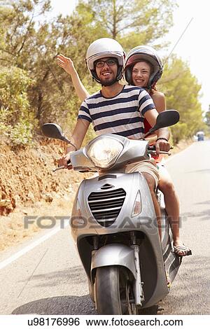 Stock Photograph - Young Couple Riding Motor Scooter Along Country Road. Fotosearch