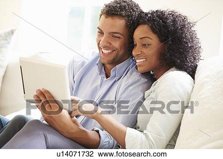 Young Couple Sitting On Sofa Using Digital Tablet View Large Photo Image Stock Image - Young Couple Sitting On Sofa Using Digital Tablet. Fotosearch