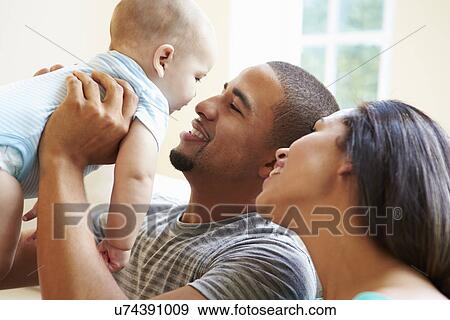 Stock Photo - Young Family Playing With Happy Baby Son At Home. Fotosearch